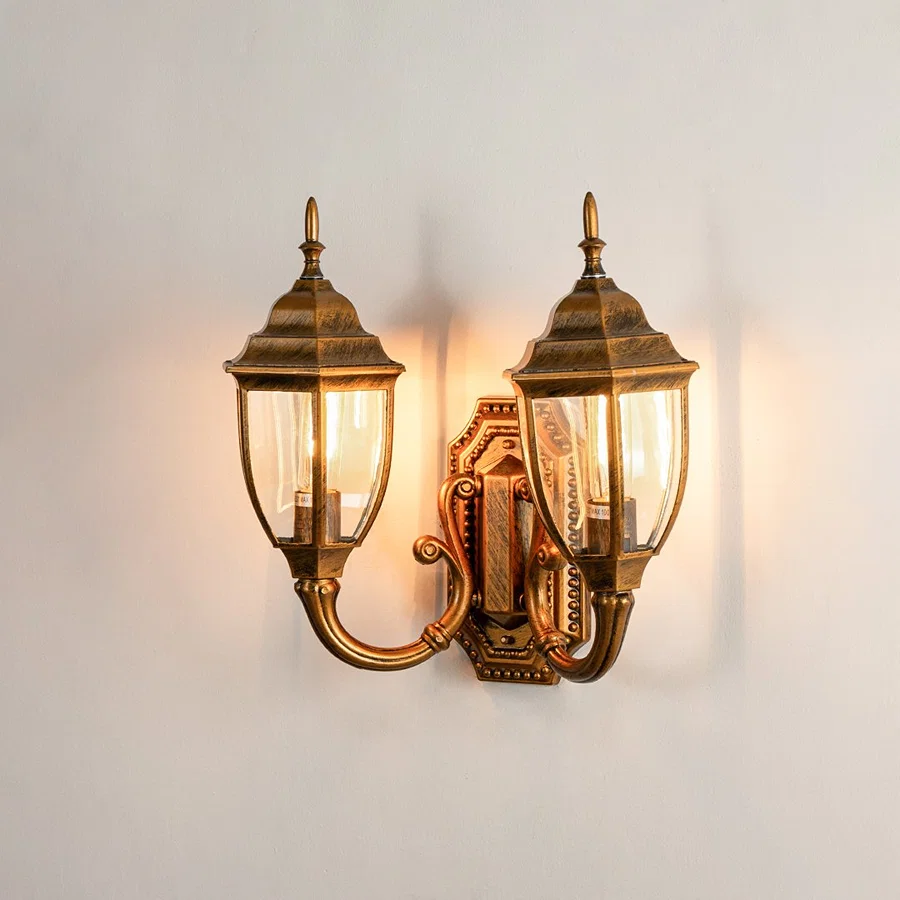 Antique brass metal double-headed outdoor wall sconce on white background with clear glass lantern shades for decor.