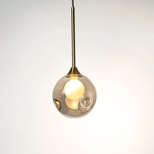 Clear glass globe pendant light with gold holder and visible bulb hanging against neutral wall background highlighting elegant contemporary lighting design.