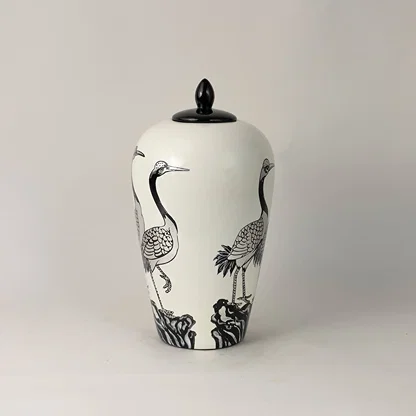 Side view of white ceramic jar with hand-painted crane pattern and black lid highlighting intricate artistic detailing.