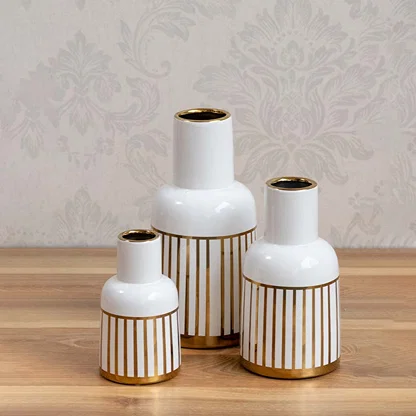 A decorative white and gold ceramic vase showcased in a styled setup emphasizing its modern striped design and elegant glossy appearance.