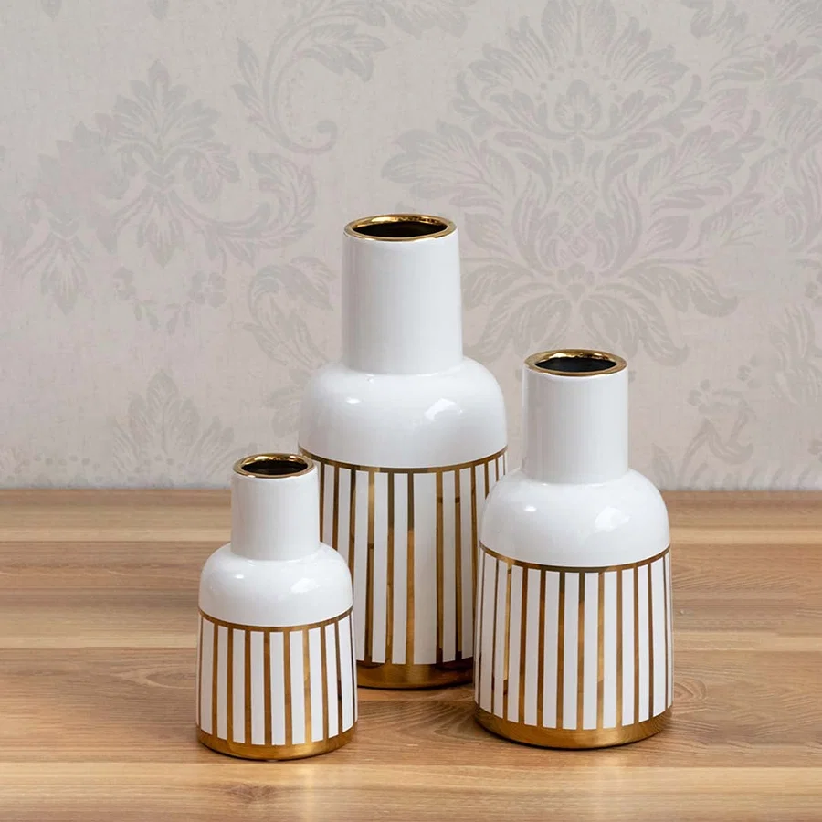 A decorative white and gold ceramic vase showcased in a styled setup emphasizing its modern striped design and elegant glossy appearance.