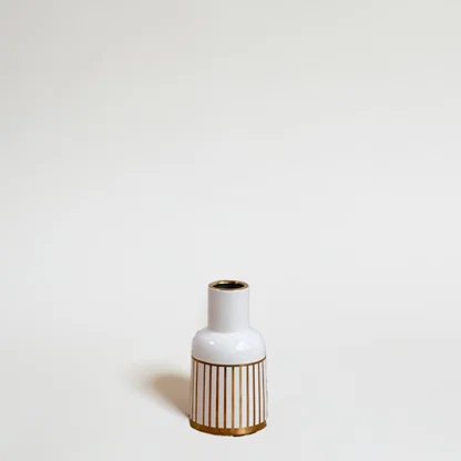 A modern ceramic vase in white with gold striped detailing photographed on a bright background emphasizing its sleek shape and artistic style.