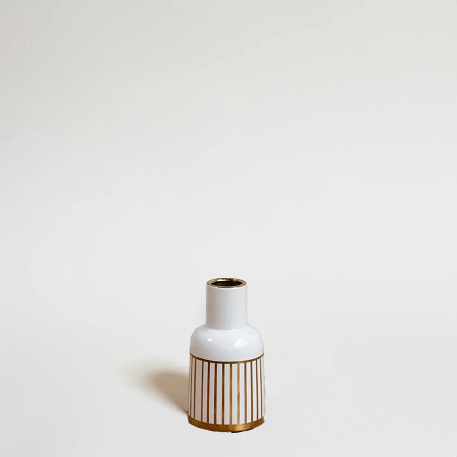 A modern ceramic vase in white with gold striped detailing photographed on a bright background emphasizing its sleek shape and artistic style.
