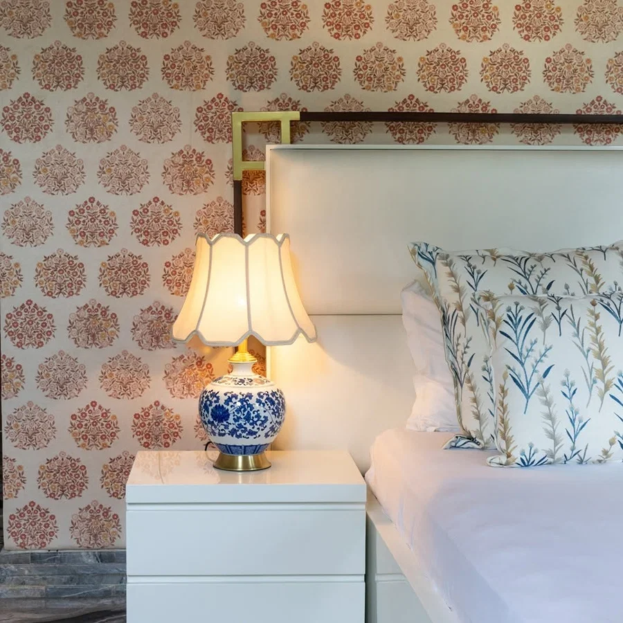 Blue floral ceramic table lamp with pleated fabric shade beside a bed creating warm classic bedroom lighting.