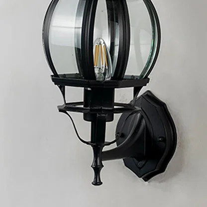 Closeup of black outdoor wall lantern showing curved glass cage panel detail and decorative finial traditional coach design.