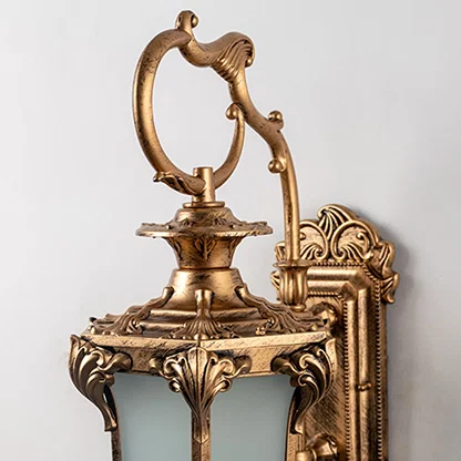 Closeup view of antique outdoor wall light with golden detailing and frosted glass for classic exterior lighting.