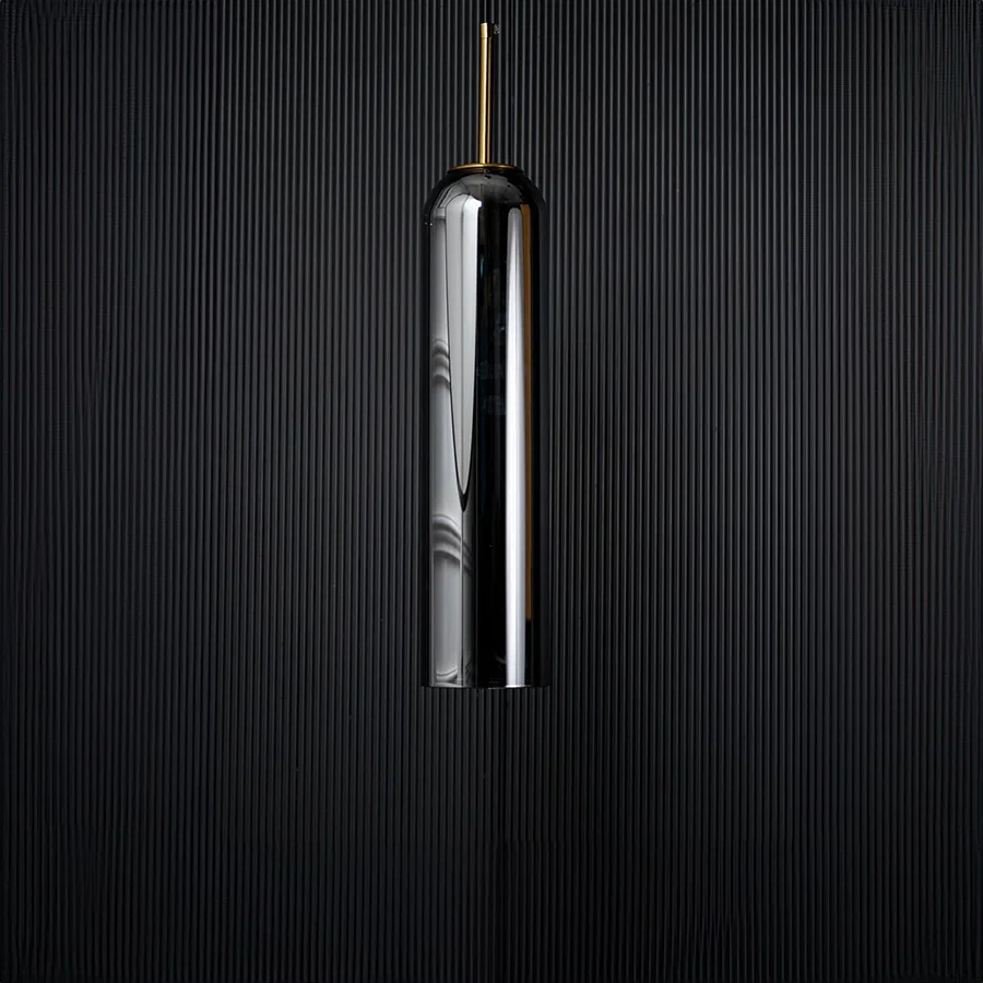 A tall silver cylindrical pendant light displayed on a black background with the light turned off emphasizing its glossy surface and slim elegant silhouette.