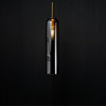 A modern silver cylindrical pendant light against a deep black background with the light turned on casting a warm glow and highlighting its reflective finish.