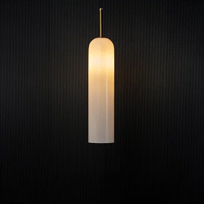A modern cylindrical pendant light with the light on illuminating softly and creating a warm halo effect against a dark black background for dramatic contrast.