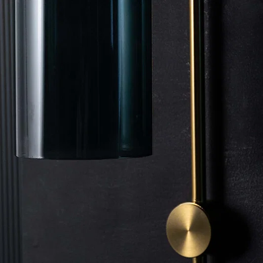 Detailed close up view of a luxury gold brass wall sconce featuring a smoky blue cylindrical glass shade fixture.