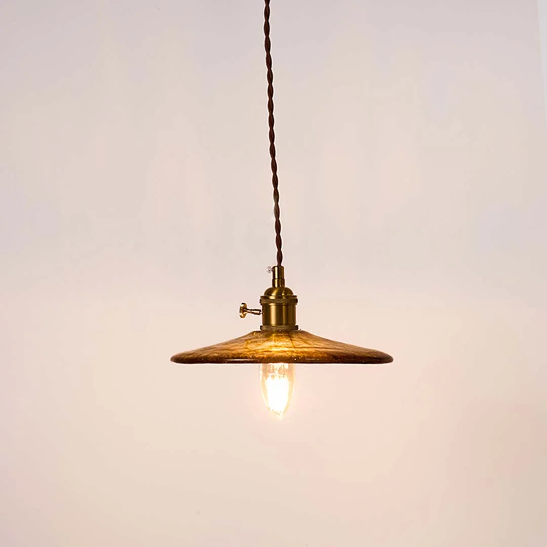 Brass metal pendant light with disc shade and exposed bulb creating warm ambient lighting indoors.