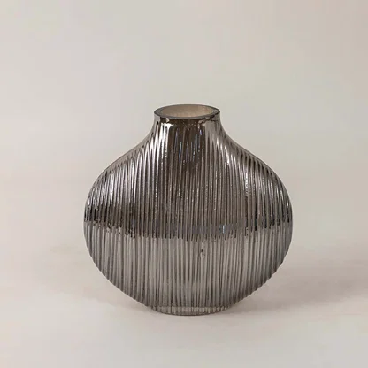 Elegant smoky glass vase with ribbed detailing and smooth round silhouette placed on a plain white surface for a minimal look.