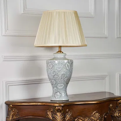 Ceramic table lamp with floral patterns and pleated shade shown on a white backdrop emphasizing its sculpted silhouette and craftsmanship.