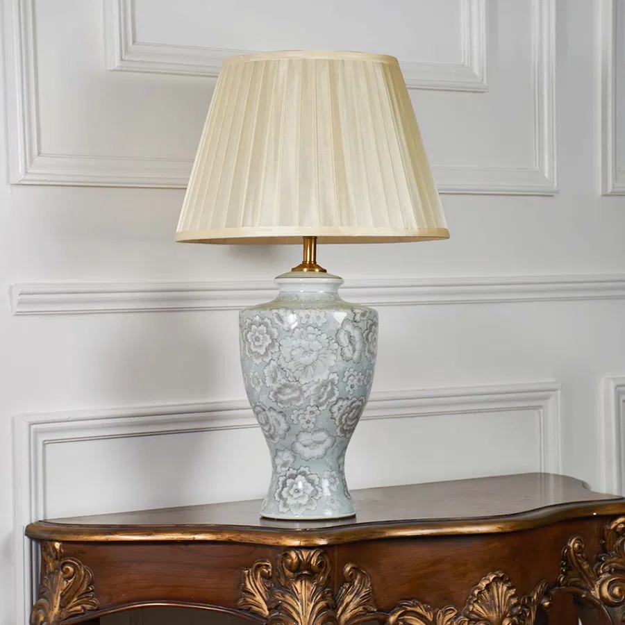 Ceramic table lamp with floral patterns and pleated shade shown on a white backdrop emphasizing its sculpted silhouette and craftsmanship.