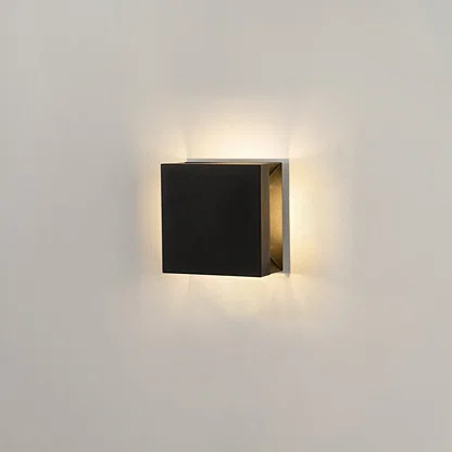 Modern square black aluminum outdoor wall sconce on white background casting warm multi-directional up and down light.