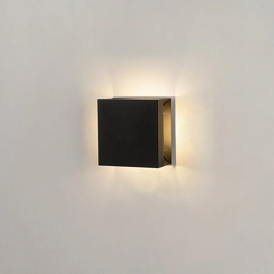 Modern square black aluminum outdoor wall sconce on white background casting warm multi-directional up and down light.