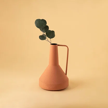 Matte orange metal vase with handle and leaf stem for modern minimalist home decor and vibrant table styling.