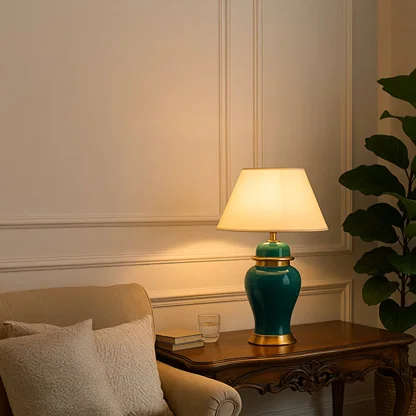 Green ceramic table lamp with golden base and white fabric shade turned on styled in elegant living room decor.