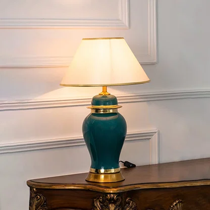 Green ceramic lamp with golden base and white shade turned on glowing against a plain white background.