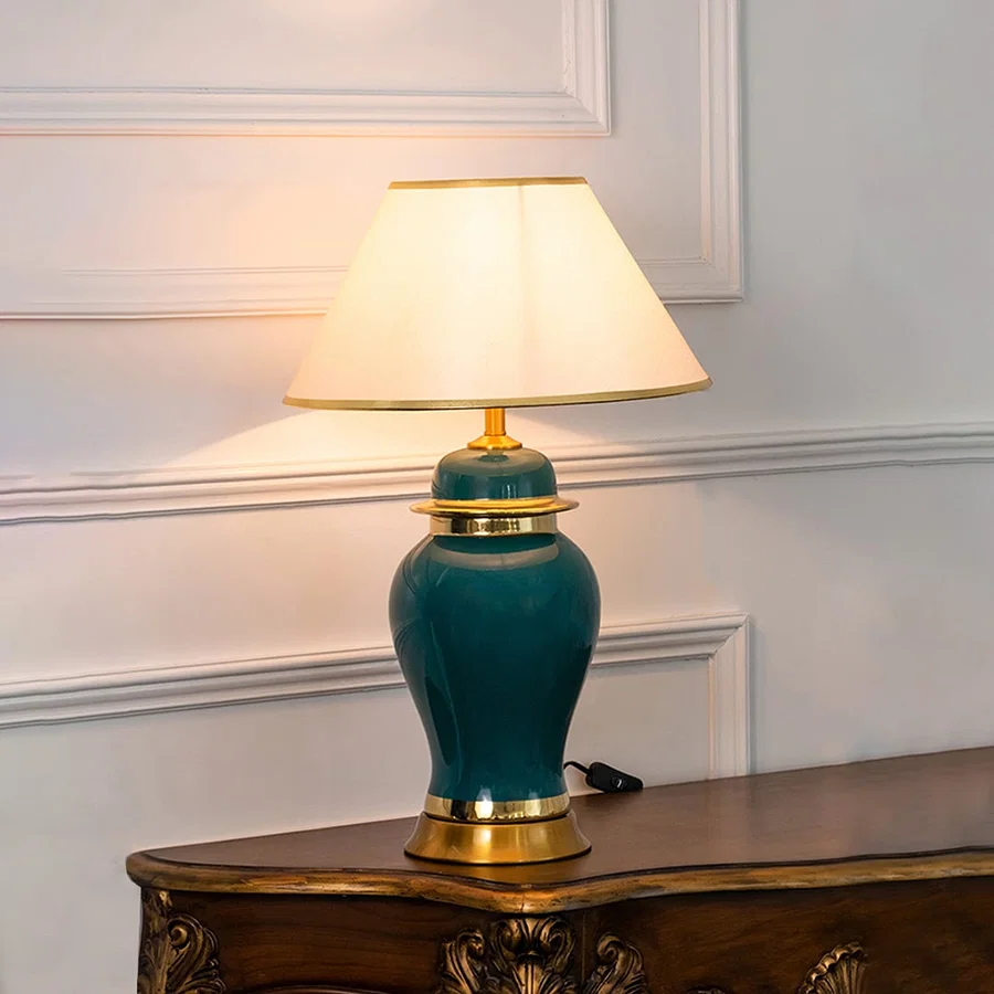 Green ceramic lamp with golden base and white shade turned on glowing against a plain white background.