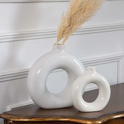 Two glossy white circular vases placed on a wooden table with soft natural decor showing elegant shapes that add a minimal and calming look to the room.