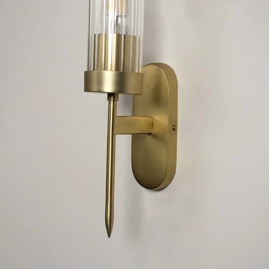 Modern brass metal wall light with clear glass cylinder shade for elegant bedroom and hallway decor.
