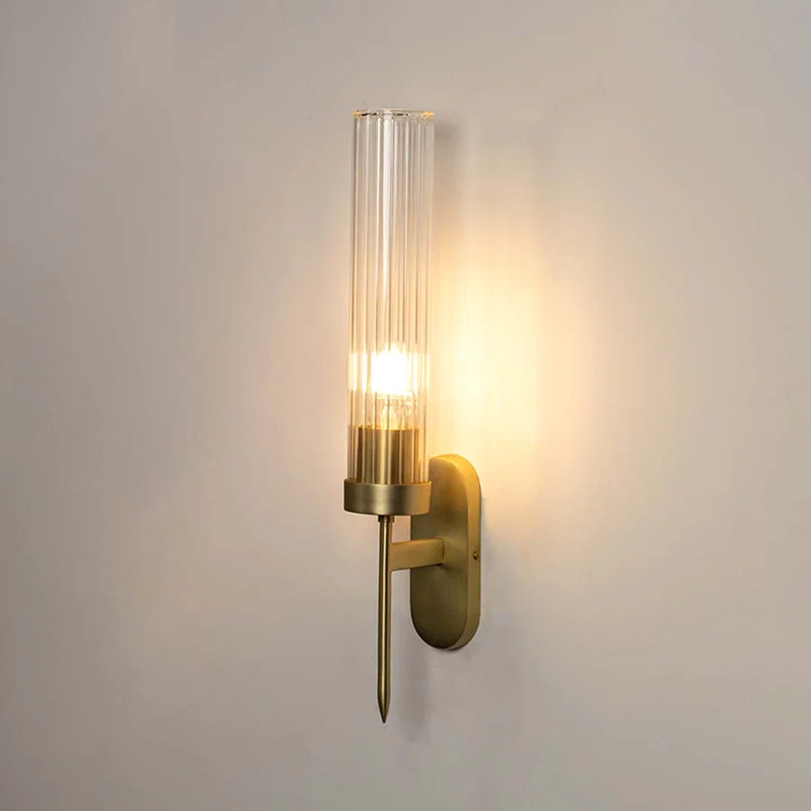 Golden wall sconce with tall clear glass shade turned on displayed on white background for modern interiors.