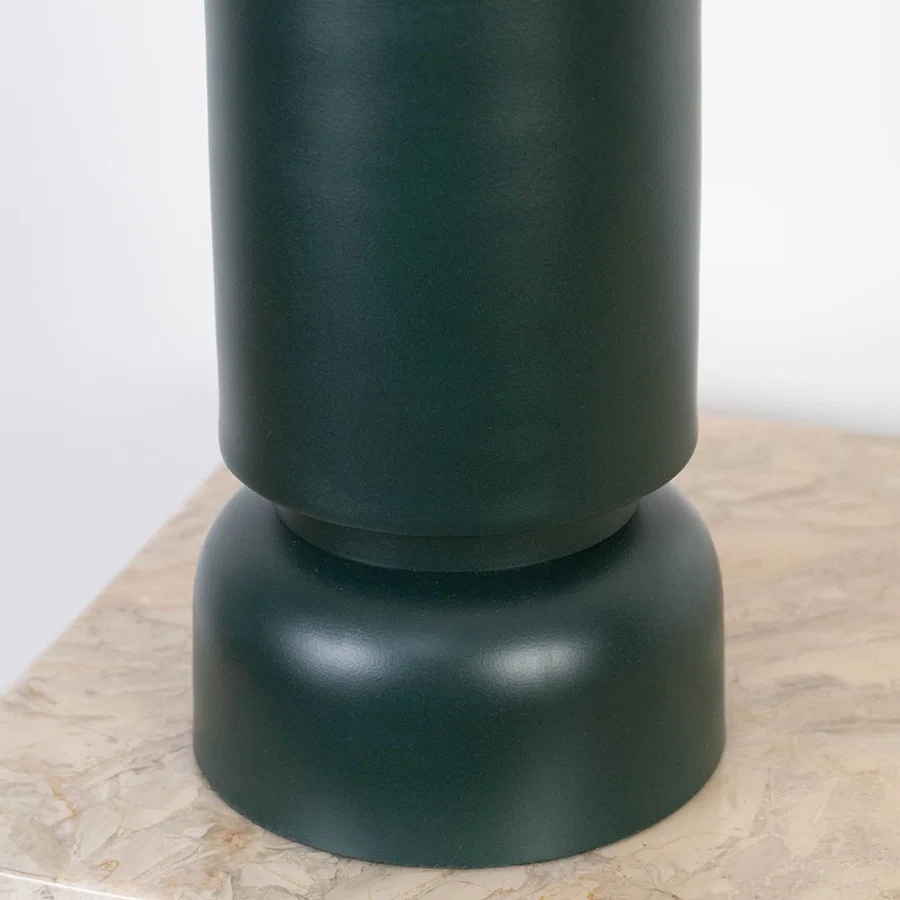 Smooth matte dark green ceramic base of table lamp shown in close-up detail on a marble surface.