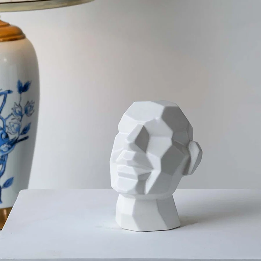 White geometric sculptures placed on wooden desk beside lamp and book enhancing elegant minimalist home setting.