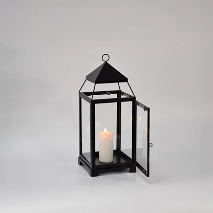 Black metal glass lantern with candle lit shown on white background highlighting warm glow classic frame design and home decor use.