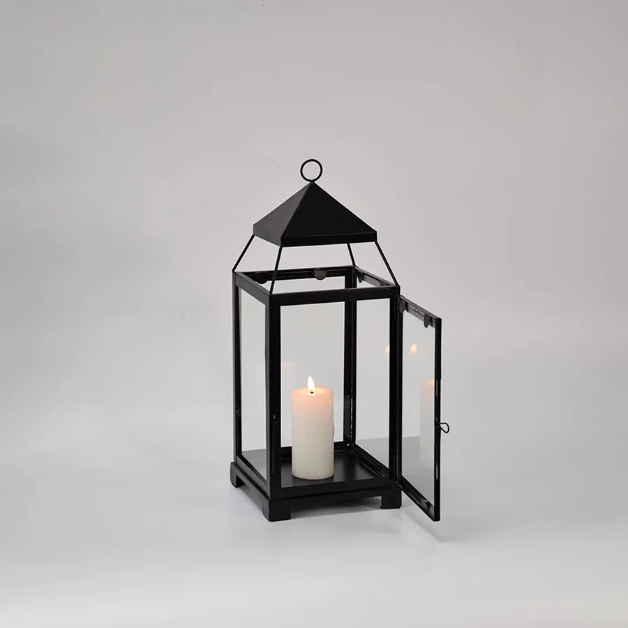 Black metal glass lantern with candle lit shown on white background highlighting warm glow classic frame design and home decor use.