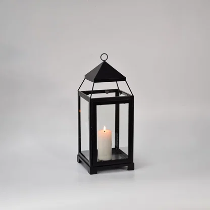 Black metal glass lantern with candle lit shown on white background highlighting warm glow classic frame design and home decor use.
