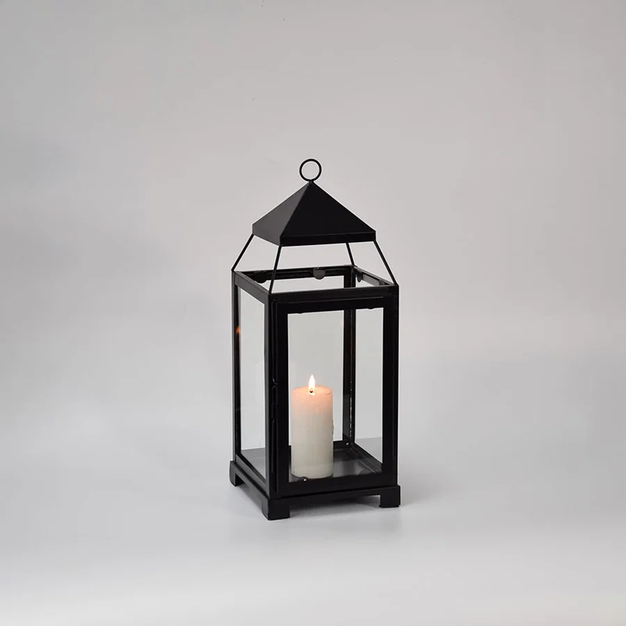 Black metal glass lantern with candle lit shown on white background highlighting warm glow classic frame design and home decor use.