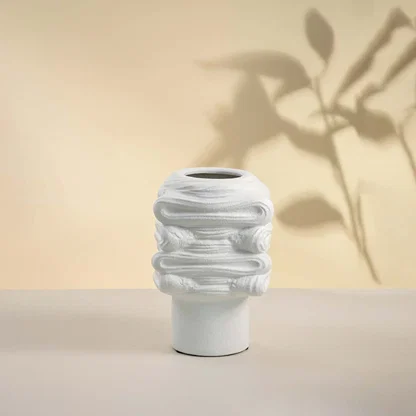 Elegant white ceramic vase placed on white background showcasing intricate surface texture and modern artistic shape.