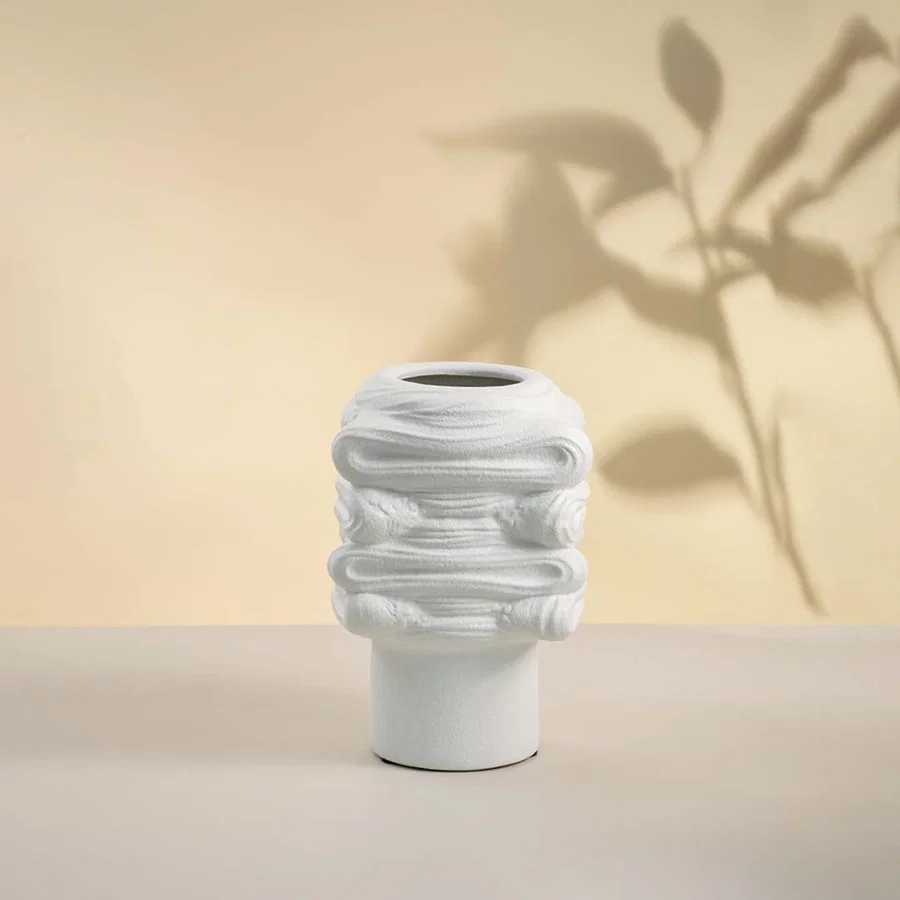 Elegant white ceramic vase placed on white background showcasing intricate surface texture and modern artistic shape.