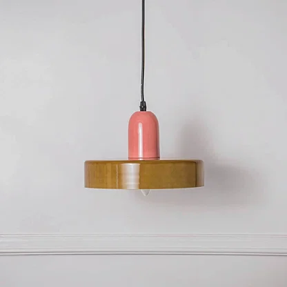 Decorative pendant light with pink holder and wooden disc shade placed against neutral wall background showcasing playful contemporary lighting design.