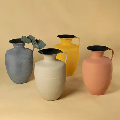 Four artisan matte metal pitcher vases with greenery for artistic home decor and stylish minimalist tabletop display.