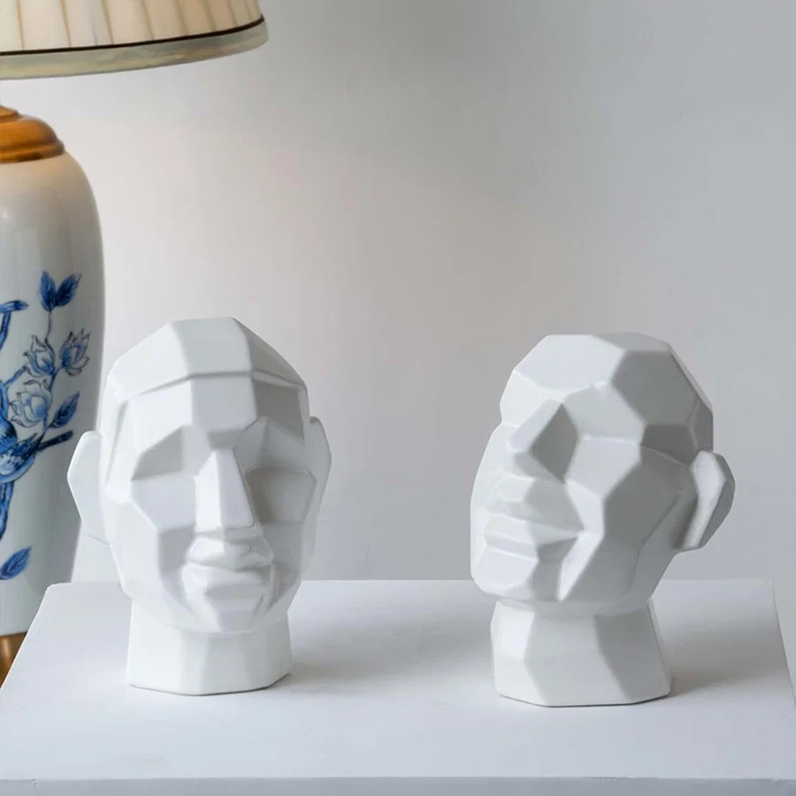 Contemporary geometric face sculpture arranged in a styled setting on a white block  emphasizing form  shadows  and artistic character.