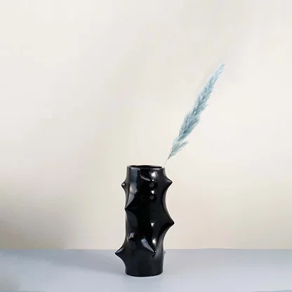Modern black ceramic vase with artistic sculptural bumps styled in a minimal home decor setup on a wooden table with soft beige wall background.