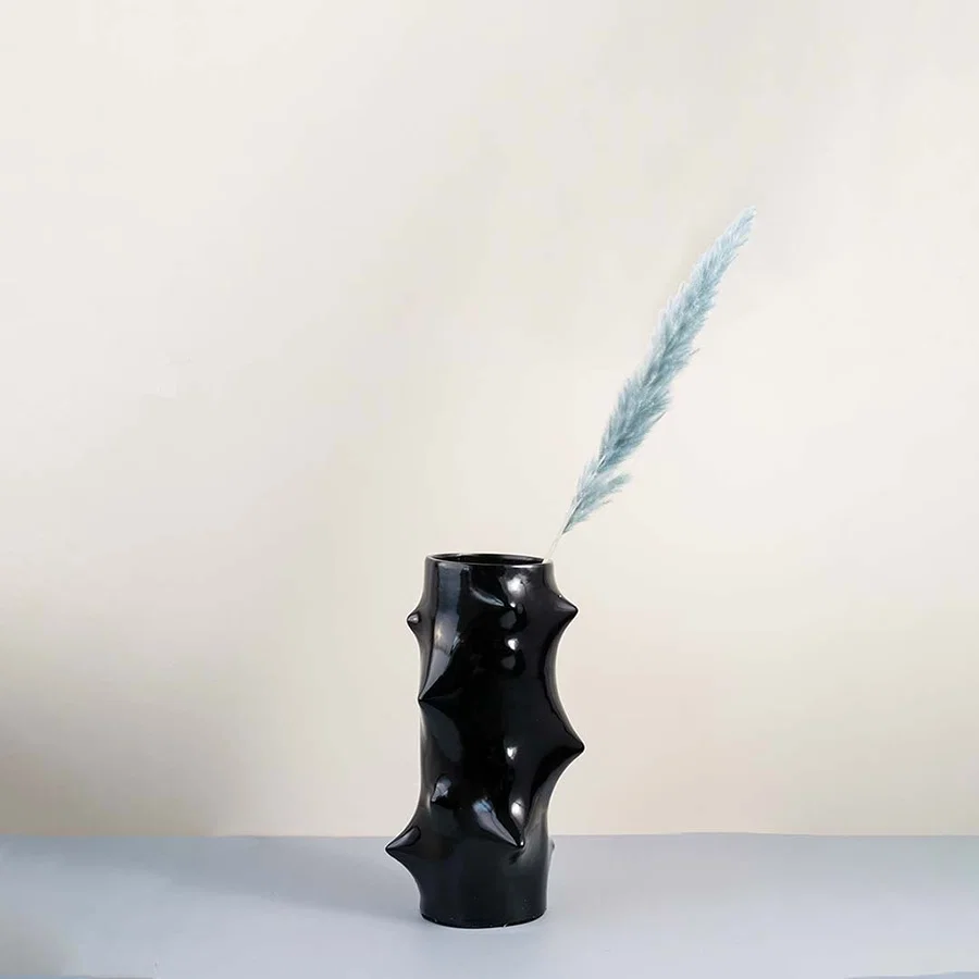 Modern black ceramic vase with artistic sculptural bumps styled in a minimal home decor setup on a wooden table with soft beige wall background.