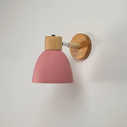 Unlit matte pink metal wall sconce with natural wood details isolated on a clean white background showcasing its simple bell shape design.