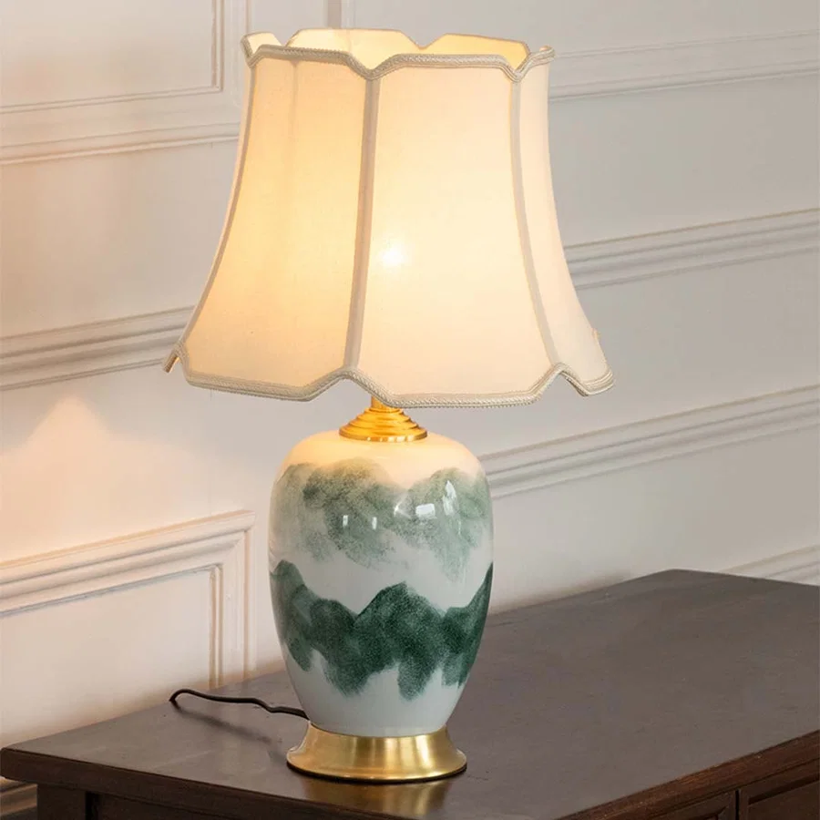 Stylish ceramic table lamp with gold base and cream shade emits a warm soft glow enhancing the beauty of its artistic blue-toned pattern.