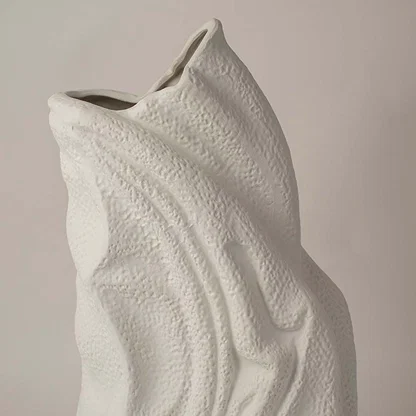 White sculptural ceramic vase closeup highlighting flowing textured surface and handcrafted organic form for contemporary interior styling.
