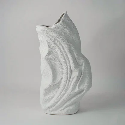 White ceramic abstract sculpture vase with flowing curved design placed on white surface against neutral background showcasing artistic modern home decor styling.