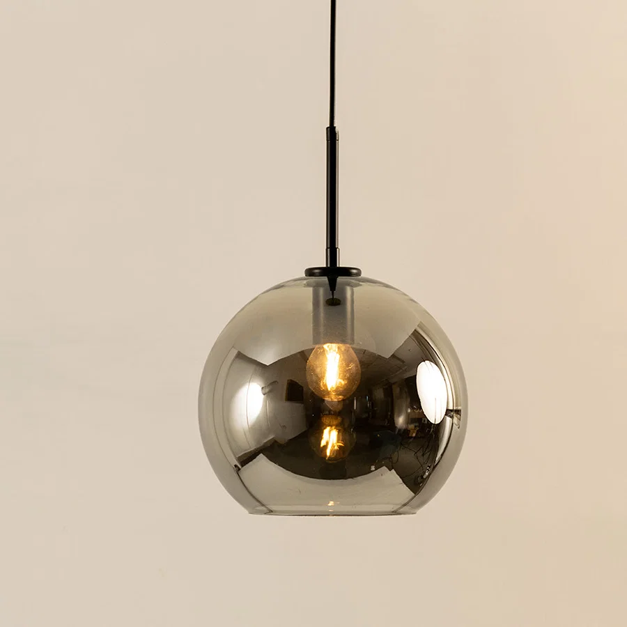 Smoky glass dome pendant light with reflective finish and hanging cord placed against neutral wall background showcasing modern luxury lighting decor styling.