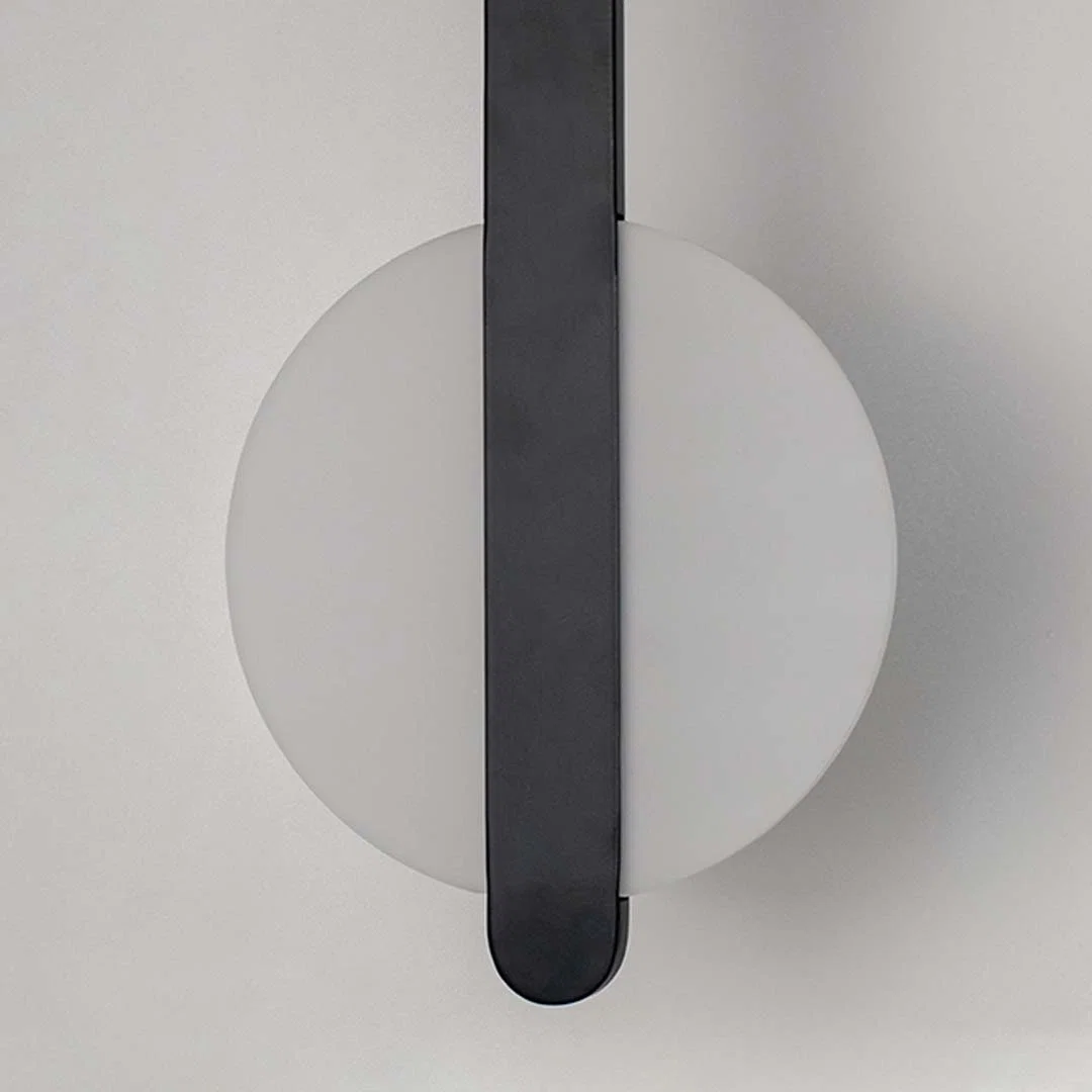 Modern wall light with white circular backplate and black vertical bar placed against neutral wall background showcasing minimal contemporary lighting decor styling.