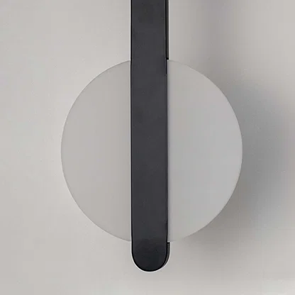 Modern wall light with white circular backplate and black vertical bar placed against neutral wall background showcasing minimal contemporary lighting decor styling.