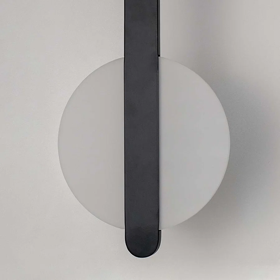 Modern wall light with white circular backplate and black vertical bar placed against neutral wall background showcasing minimal contemporary lighting decor styling.