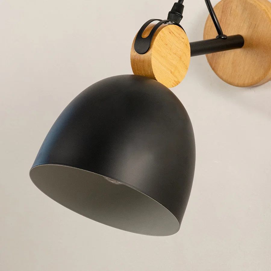 Closeup of black metal wall light with wooden backplate highlighting matte finish and design detail for modern interior wall decor.