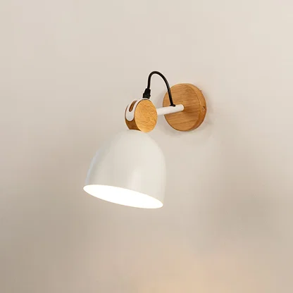 Minimalist matte white and natural wood dome wall sconce turned on against a plain background casting a warm glow downwards.